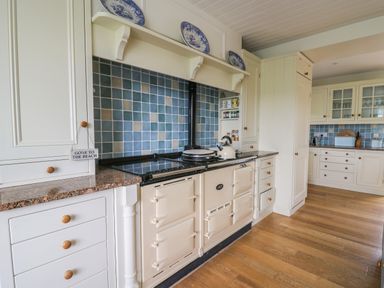 A kitchen with cream cabinets blue tiled backsplash wooden floor and a cream Aga stove at Pen y Graig in Aberporth