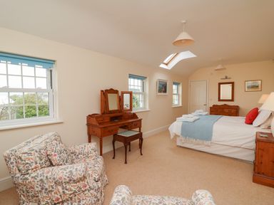 A bedroom with a bed a wooden dressing table two floral armchairs and a skylight window at Pen y Graig in Aberporth