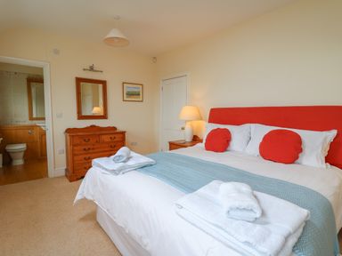 A bedroom with a bed with red headboard and pillows and folded towels on the bed at Pen y Graig in Aberporth