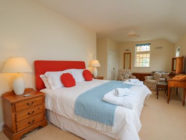 A bedroom with a bed with red cushions and a blue throw with wooden bedside tables and lamps at Pen y Graig in Aberporth