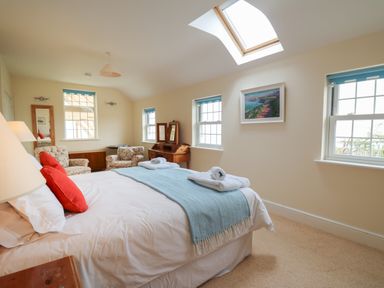 A bedroom with a bed towels armchairs a wooden dressing table and skylight at Pen y Graig in Aberporth