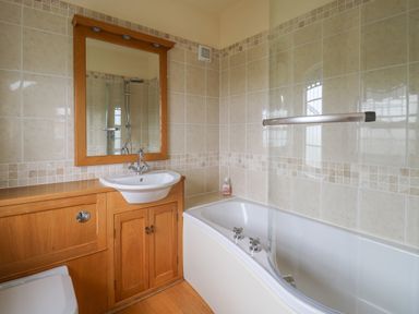 A bathroom with a wooden vanity with a white sink and mirror and a bathtub with a glass shower screen at Pen y Graig in Aberporth