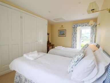 A bedroom with two single beds white closets and a window with floral curtains at Pen y Graig in Aberporth