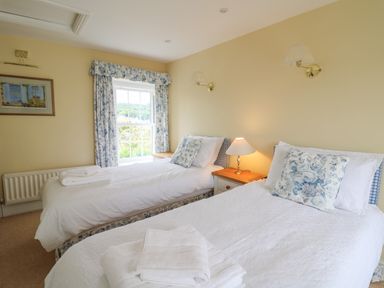 A bedroom with two single beds dressed with white linens and floral cushions at Pen y Graig in Aberporth