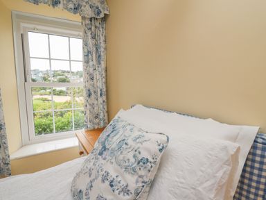 A bedroom with a window and floral curtains next to a bed with white and floral pillows at Pen y Graig in Aberporth
