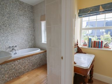 A bathroom with a bathtub and sink and a room with a wooden desk and books on the windowsill at Pen y Graig in Aberporth