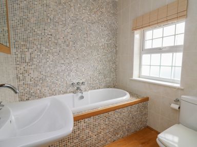 A bathroom with a bathtub tiled in mosaic next to a sink and toilet by a window at Pen y Graig in Aberporth