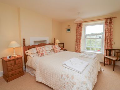 A bedroom with a double bed, bedside tables with lamps, two chairs, curtains, and a window at Pen y Graig in Aberporth