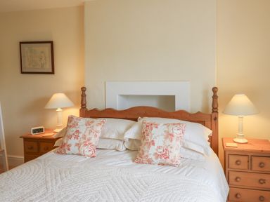 A bedroom with a wooden bed frame white bedding floral pillows two wooden nightstands with lamps and a framed picture on the wall at Pen y Graig in Aberporth