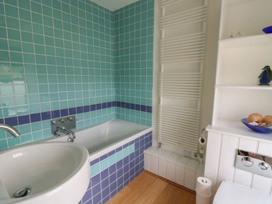 A bathroom with a bathtub tiled in blue and turquoise tiles a white sink wooden floor and a white heated towel rail at Pen y Graig in Aberporth