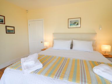 A bedroom with a double bed white bedding folded towels on the bed bedside lamps and framed pictures on walls at Pen y Graig in Aberporth