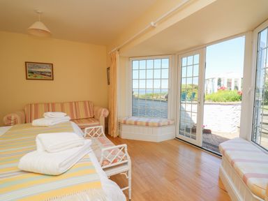 A bedroom with a bed with striped blanket and towels a striped sofa and large windows with seating at Pen y Graig in Aberporth