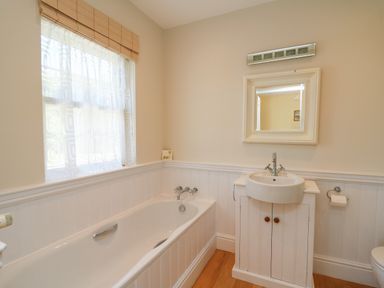 A bathroom with a bathtub a sink with cabinet a mirror and a window at Pen y Graig in Aberporth