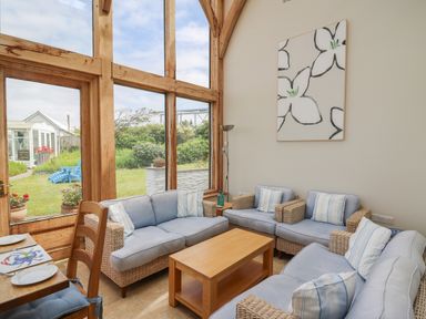 A living room with light blue cushioned wicker sofas a wooden coffee table and large wooden framed windows at Pen y Graig in Aberporth