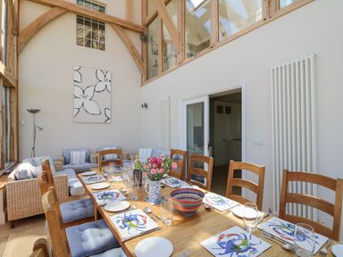 A dining room with a wooden table set with plates and crab-themed mats and a seating area with woven armchairs at Pen y Graig in Aberporth