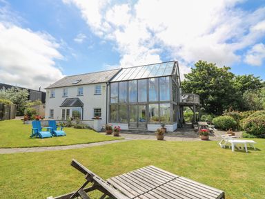 A garden with lounge chairs and a two-story house with a large glass conservatory at Pen y Graig in Aberporth