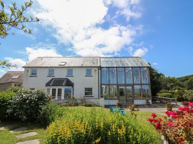 A white two-story house with a glass sunroom and garden with flowers and outdoor seating at Pen y Graig in Aberporth
