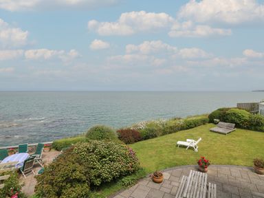 A garden with lawn chairs and tables overlooking the sea at Pen y Graig in Aberporth