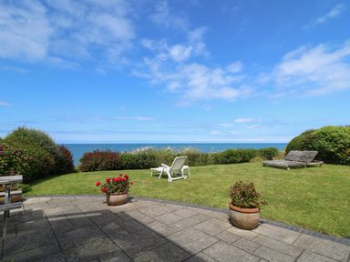 A garden with lawn chairs and potted plants overlooking the ocean at Pen y Graig in Aberporth