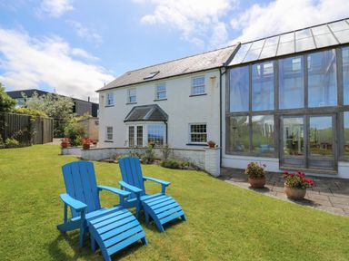 A garden with two blue chairs and a white house with a large glass sunroom at Pen y Graig in Aberporth