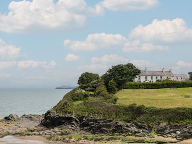 A rocky coastline with grass and trees and a row of white houses at Pen y Graig in Aberporth