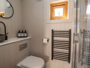 A bathroom with a toilet a black towel rack a small window and toiletries on a shelf at Cariad Mawr in Gwaenysgor near Prestatyn