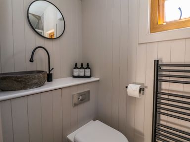 A bathroom with a round mirror stone sink and wall-mounted toilet at Cariad Mawr in Gwaenysgor near Prestatyn