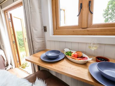 A wooden table with blue plates and bowls with food and a glass of white wine by a window at Cariad Mawr in Gwaenysgor near Prestatyn