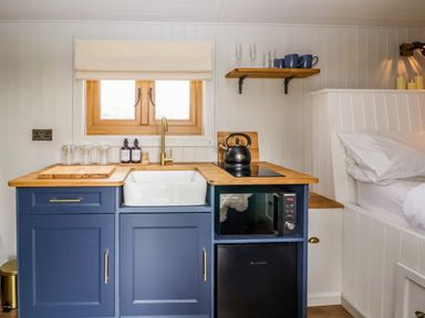 A small kitchen area with blue cabinets a white sink a microwave a black kettle and wooden countertops at Cariad Mawr in Gwaenysgor near Prestatyn