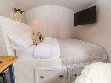 A small bedroom with a bed white bedding a wall-mounted TV and storage drawers below the bed at Cariad Mawr in Gwaenysgor near Prestatyn