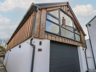 An exterior view of a building with wooden upper cladding large windows and a black roller door at Cuckoo's Rest in Penryn
