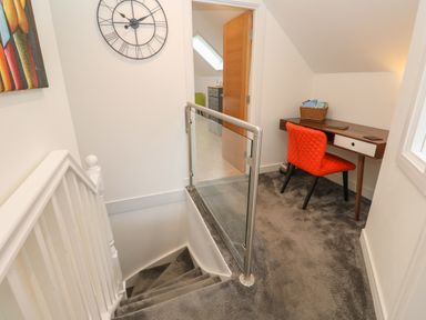 Stairs with grey carpet leading to a small workspace with a wooden desk and red chair at Cuckoo's Rest in Penryn
