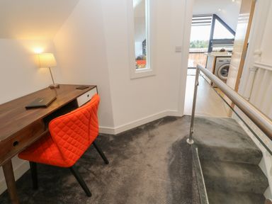 An upstairs hallway with a wooden desk and orange chair next to a lamp and a view into a kitchen with a washing machine at Cuckoo's Rest in Penryn