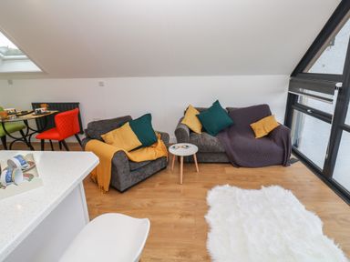 A living room with two gray sofas with colored cushions next to a small white table and a white fluffy rug at Cuckoo's Rest in Penryn