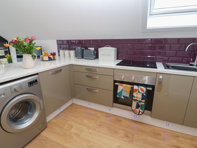 A kitchen with washing machine, oven, sink, toaster, kettle, bread bin, flowers, and fruit bowl at Cuckoo's Rest in Penryn