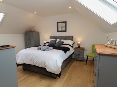 A bedroom with a bed pillows bedside tables a wardrobe a chair and dressers at Cuckoo's Rest in Penryn