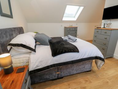 A bedroom with a bed pillows and blankets bedside tables dressers a skylight window and a wall mounted tv at Cuckoo's Rest in Penryn