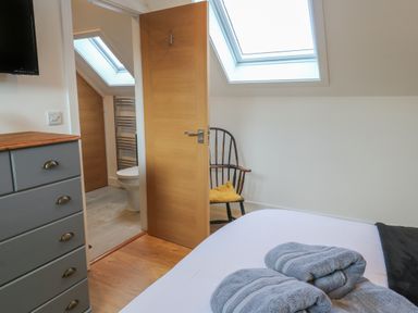 A bedroom with a bed and towels with a wooden chair and an open door leading to a bathroom with a toilet at Cuckoo's Rest in Penryn