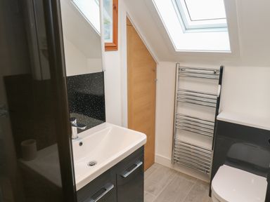 A bathroom with a white sink, black vanity, towel rack, toilet, wooden door, and skylight window at Cuckoo's Rest in Penryn