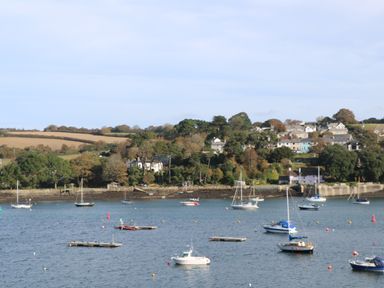 A body of water with several boats and floating docks near a shoreline with trees and houses at Cuckoo's Rest in Penryn