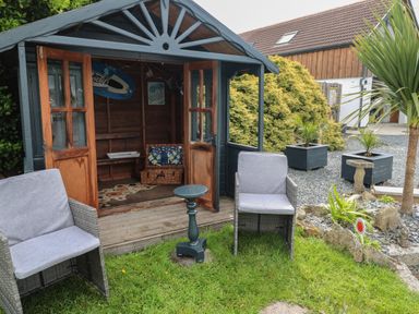 An outdoor seating area with two chairs and a small table next to a wooden garden shed with open doors at Cuckoo's Rest in Penryn