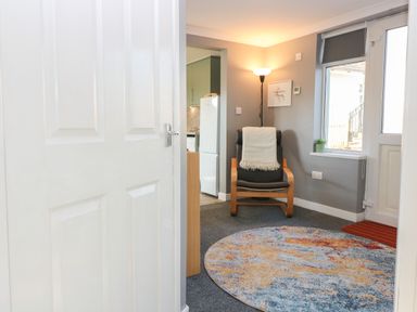 A sitting area with a wooden armchair with a blanket a round colorful rug a floor lamp and a window at Caldwell Cottage in Lanark