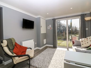 A living room with a wall-mounted television and large sliding glass doors leading outside at Caldwell Cottage in Lanark