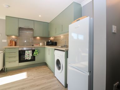 A kitchen with green cabinets a white refrigerator a washing machine and a countertop with appliances at Caldwell Cottage in Lanark
