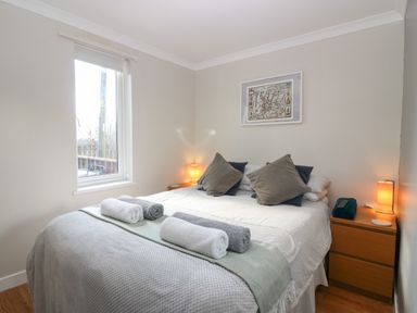 A bedroom with a double bed with rolled towels on it two bedside tables with lamps and a window at Caldwell Cottage in Lanark