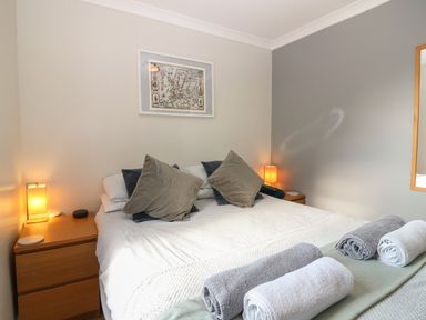 A bedroom with a double bed featuring multiple pillows and rolled towels on top at Caldwell Cottage in Lanark