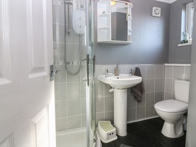 A bathroom with a shower enclosure a pedestal sink a toilet and a small window at Caldwell Cottage in Lanark