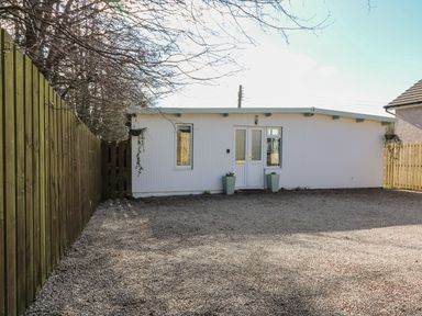 A single story white building with a gravel yard and wooden fences on both sides at Caldwell Cottage in Lanark