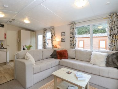 A living room with a beige sectional sofa and throw pillows a wooden coffee table with books and flowers on a table at No 3 Foxburrow Hang in Belton