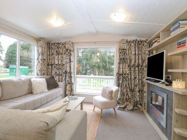 A living room with sofas a small chair a coffee table a television on a wooden shelf and large windows with patterned curtains at No 3 Foxburrow Hang in Belton